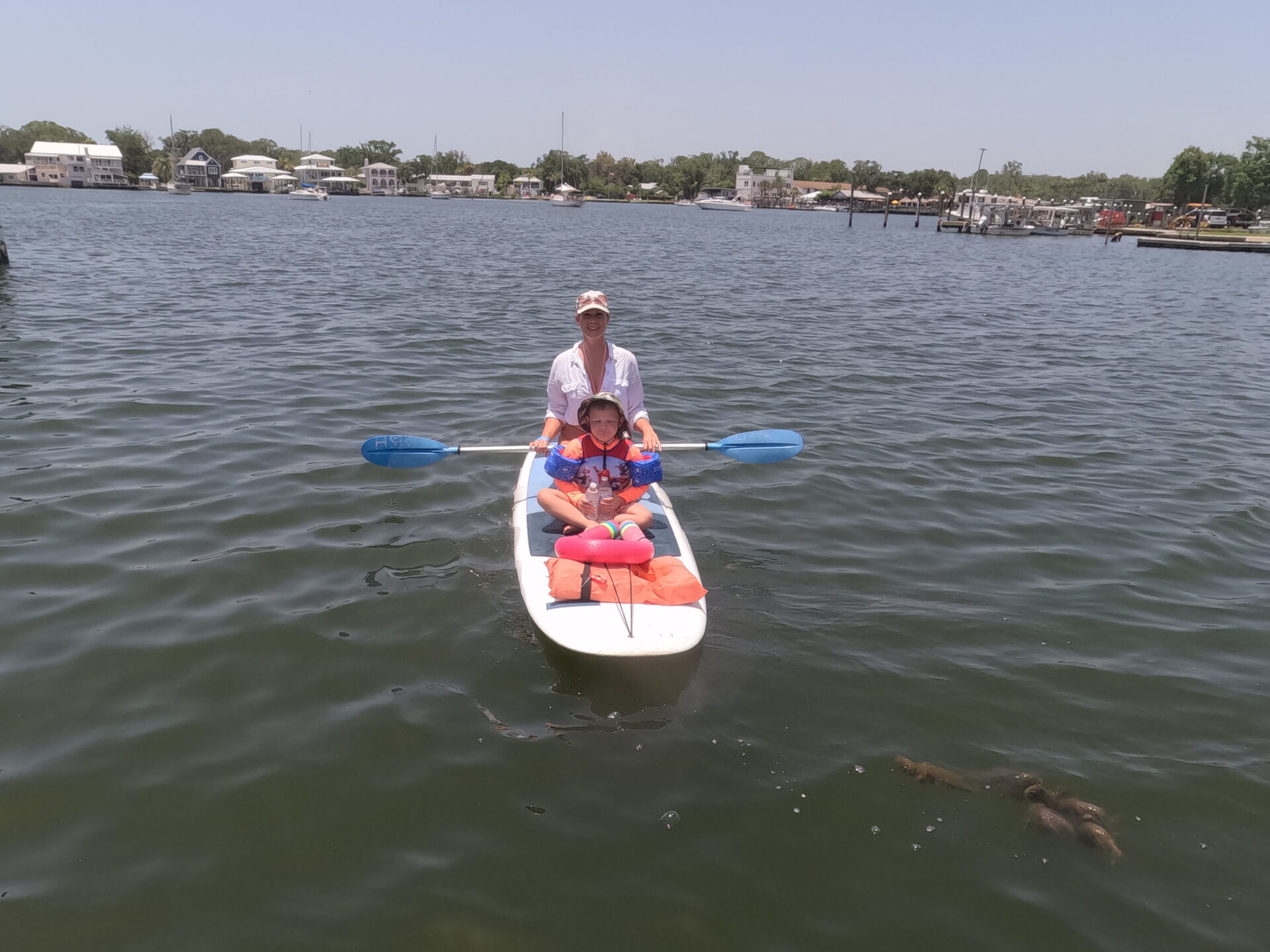 An adult and child sharing a paddleboard on open water